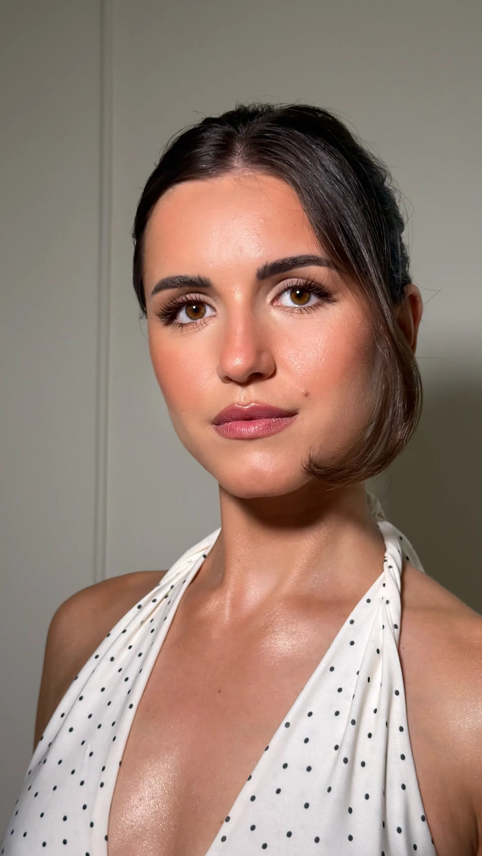 Mise en beauté lumineuse : teint glowy, regard brun intense et lèvres rosées, cheveux bruns tirés en arrière