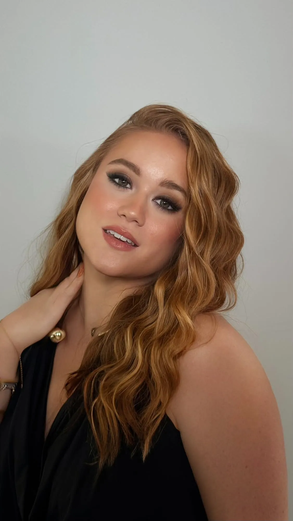Femme aux longs cheveux cuivrés ondulés, regard smoky brun et lèvres nude, main posée sur la nuque